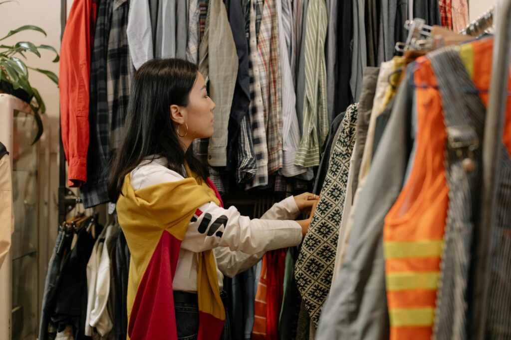 A young woman browsing clothes in a vintage store with colorful outfits.